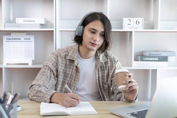 Hombre Asiático Tomando Notas Cuaderno Mientras Estudia Línea Ordenador Portátil —  Fotos de Stock