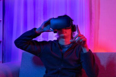 Sanal gerçeklik gözlüğü takan adam heyecan verici bir 3 boyutlu oyun oynuyor, Bluetooth Uzaktan Kumanda, VR, Gelecek Oyunları, Gadget, Teknoloji, Kırmızı ve Mavi arka plan, VR oyun konsepti.