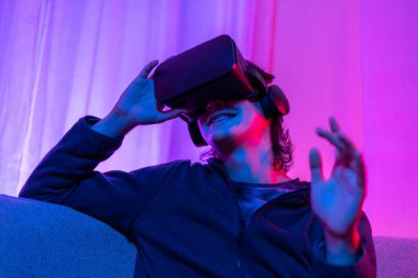 Sanal gerçeklik gözlüğü takan adam heyecan verici bir 3 boyutlu oyun oynuyor, Bluetooth Uzaktan Kumanda, VR, Gelecek Oyunları, Gadget, Teknoloji, Kırmızı ve Mavi arka plan, VR oyun konsepti.