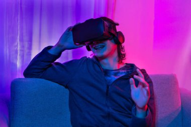 Sanal gerçeklik gözlüğü takan adam heyecan verici bir 3 boyutlu oyun oynuyor, Bluetooth Uzaktan Kumanda, VR, Gelecek Oyunları, Gadget, Teknoloji, Kırmızı ve Mavi arka plan, VR oyun konsepti.