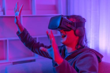 Sanal gerçeklik gözlüğü takan adam heyecan verici bir 3 boyutlu oyun oynuyor, Bluetooth Uzaktan Kumanda, VR, Gelecek Oyunları, Gadget, Teknoloji, Kırmızı ve Mavi arka plan, VR oyun konsepti.