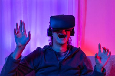 Sanal gerçeklik gözlüğü takan adam heyecan verici bir 3 boyutlu oyun oynuyor, Bluetooth Uzaktan Kumanda, VR, Gelecek Oyunları, Gadget, Teknoloji, Kırmızı ve Mavi arka plan, VR oyun konsepti.