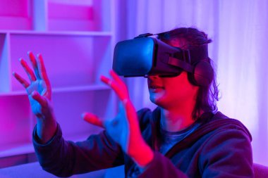 Sanal gerçeklik gözlüğü takan adam heyecan verici bir 3 boyutlu oyun oynuyor, Bluetooth Uzaktan Kumanda, VR, Gelecek Oyunları, Gadget, Teknoloji, Kırmızı ve Mavi arka plan, VR oyun konsepti.