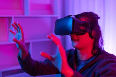 Sanal gerçeklik gözlüğü takan adam heyecan verici bir 3 boyutlu oyun oynuyor, Bluetooth Uzaktan Kumanda, VR, Gelecek Oyunları, Gadget, Teknoloji, Kırmızı ve Mavi arka plan, VR oyun konsepti.