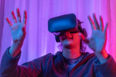 Sanal gerçeklik gözlüğü takan adam heyecan verici bir 3 boyutlu oyun oynuyor, Bluetooth Uzaktan Kumanda, VR, Gelecek Oyunları, Gadget, Teknoloji, Kırmızı ve Mavi arka plan, VR oyun konsepti.