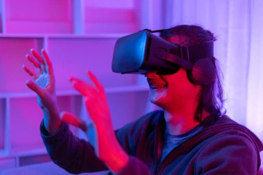 Sanal gerçeklik gözlüğü takan adam heyecan verici bir 3 boyutlu oyun oynuyor, Bluetooth Uzaktan Kumanda, VR, Gelecek Oyunları, Gadget, Teknoloji, Kırmızı ve Mavi arka plan, VR oyun konsepti.