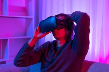 Sanal gerçeklik gözlüğü takan adam heyecan verici bir 3 boyutlu oyun oynuyor, Bluetooth Uzaktan Kumanda, VR, Gelecek Oyunları, Gadget, Teknoloji, Kırmızı ve Mavi arka plan, VR oyun konsepti.