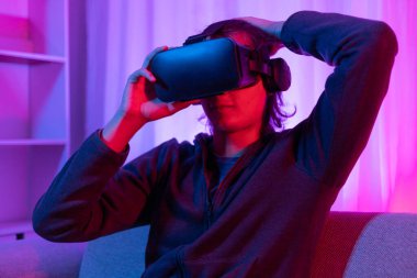 Sanal gerçeklik gözlüğü takan adam heyecan verici bir 3 boyutlu oyun oynuyor, Bluetooth Uzaktan Kumanda, VR, Gelecek Oyunları, Gadget, Teknoloji, Kırmızı ve Mavi arka plan, VR oyun konsepti.