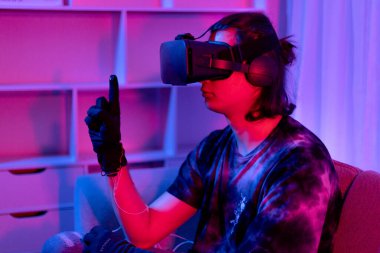 Sanal gerçeklik gözlüğü takan adam heyecan verici bir 3 boyutlu oyun oynuyor, Bluetooth Uzaktan Kumanda, VR, Gelecek Oyunları, Gadget, Teknoloji, Kırmızı ve Mavi arka plan, VR oyun konsepti.