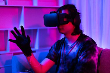 Sanal gerçeklik gözlüğü takan adam heyecan verici bir 3 boyutlu oyun oynuyor, Bluetooth Uzaktan Kumanda, VR, Gelecek Oyunları, Gadget, Teknoloji, Kırmızı ve Mavi arka plan, VR oyun konsepti.