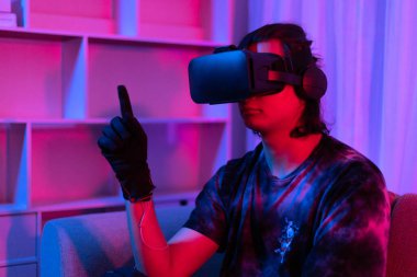 Sanal gerçeklik gözlüğü takan adam heyecan verici bir 3 boyutlu oyun oynuyor, Bluetooth Uzaktan Kumanda, VR, Gelecek Oyunları, Gadget, Teknoloji, Kırmızı ve Mavi arka plan, VR oyun konsepti.