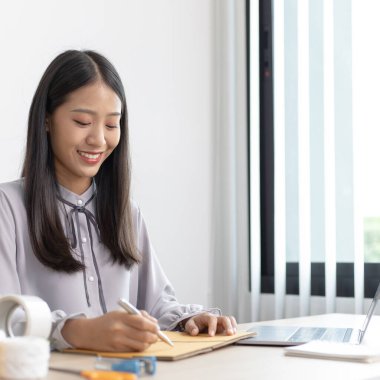 Asyalı iş kadını bir dizüstü bilgisayardan sipariş alıyor ve siparişlerini doğrulamak, ürünleri İnternet 'te satmak veya ev konseptinde serbest iş yapmak için müşterilerle sohbet ediyor..