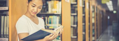 Asyalı kız öğrenciler kütüphanede okuyor ve okuyor, kütüphanede öğreniyorlar.