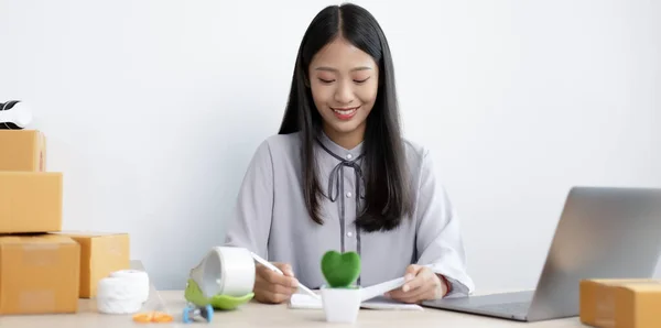 Asian businesswoman is taking online orders from a laptop and chatting with customers to confirm their order, Selling products online or doing freelance work at home concept.