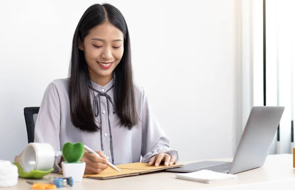 Asian businesswoman is taking online orders from a laptop and chatting with customers to confirm their order, Selling products online or doing freelance work at home concept.