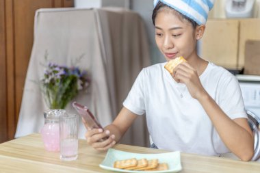 Asyalı kadın kahvaltısını kraker (sağlıklı tam tahıl) ve meyve suyu ile yer, telefonunuzu ya da cep telefonunuzu sabah haberlerini aramak için kullanın, apartman zemininde küçük bir oda, uyandırma aktiviteleri.