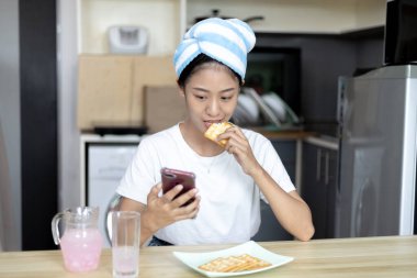 Asyalı kadın kahvaltısını kraker (sağlıklı tam tahıl) ve meyve suyu ile yer, telefonunuzu ya da cep telefonunuzu sabah haberlerini aramak için kullanın, apartman zemininde küçük bir oda, uyandırma aktiviteleri.