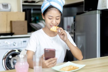 Asyalı kadın kahvaltısını kraker (sağlıklı tam tahıl) ve meyve suyu ile yer, telefonunuzu ya da cep telefonunuzu sabah haberlerini aramak için kullanın, apartman zemininde küçük bir oda, uyandırma aktiviteleri.