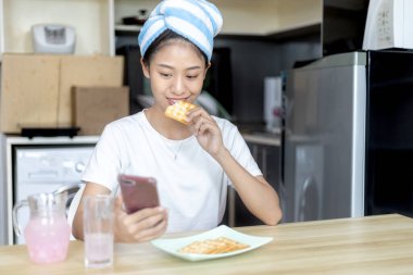 Asyalı kadın kahvaltısını kraker (sağlıklı tam tahıl) ve meyve suyu ile yer, telefonunuzu ya da cep telefonunuzu sabah haberlerini aramak için kullanın, apartman zemininde küçük bir oda, uyandırma aktiviteleri.