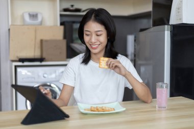 Asyalı kadın kahvaltısını kraker (sağlıklı tam tahıl) ve meyve suyu ile yer, telefonunuzu ya da tabletinizi sabah haberlerini aramak için kullanın, apartman zemininde küçük bir oda, uyandırma aktiviteleri
