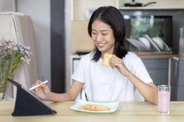 Asyalı kadın kahvaltısını kraker (sağlıklı tam tahıl) ve meyve suyu ile yer, telefonunuzu ya da tabletinizi sabah haberlerini aramak için kullanın, apartman zemininde küçük bir oda, uyandırma aktiviteleri