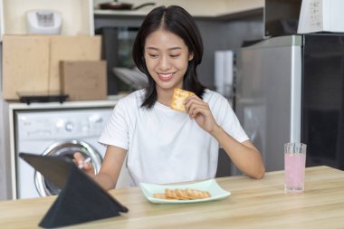 Asyalı kadın kahvaltısını kraker (sağlıklı tam tahıl) ve meyve suyu ile yer, telefonunuzu ya da tabletinizi sabah haberlerini aramak için kullanın, apartman zemininde küçük bir oda, uyandırma aktiviteleri