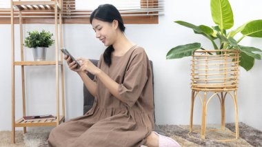 Genç Asyalı kadın cep telefonunu arkadaşlarıyla sohbet etmek ya da konuşmak, cep telefonu teknolojisini kullanarak eğlenmek ya da dinlenmek, hafta sonu evde kalmak, mutlu bir yaşam tarzı....