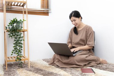 Genç Asyalı kadın bilgisayarını arkadaşlarıyla sohbet etmek ya da konuşmak, bilgisayar teknolojisi kullanarak eğlenmek ya da dinlenmek, hafta sonu boyunca evde kalmak, mutlu bir yaşam tarzı....