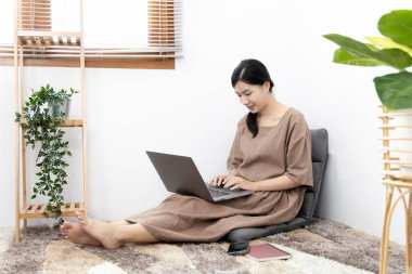 Genç Asyalı kadın bilgisayarını arkadaşlarıyla sohbet etmek ya da konuşmak, bilgisayar teknolojisi kullanarak eğlenmek ya da dinlenmek, hafta sonu boyunca evde kalmak, mutlu bir yaşam tarzı....