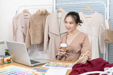 Profesyonel tasarımcı masasında oturmuş stüdyosunda moda tasarımı, moda tasarımcısı, yaratıcılık ve fikirler, manken eskizi, renk şeması, giysi aksesuarları hakkında düşünüyor..
