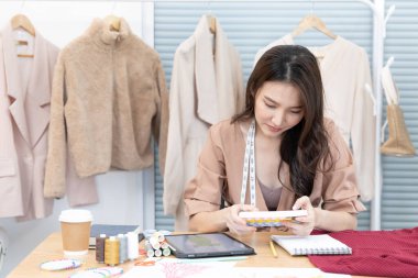 Profesyonel tasarımcı masasında oturmuş stüdyosunda moda tasarımı, moda tasarımcısı, yaratıcılık ve fikirler, manken eskizi, renk şeması, giysi aksesuarları hakkında düşünüyor..