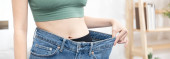 Women show a reduced or thinned waistline, Losing weight and exercising can reduce belly fat and excess fat, Loosing weight by keeping diet, Loose jeans, Body slim, Thin waist wearing big.