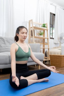 İnce Asyalı kadın evde yoga meditasyonu yapıyor, vücudun kaslarını esnetiyor ve düzgün nefes alma egzersizleri yapıyor, yoga stüdyosu, spor kıyafeti, sağlıklı yaşam tarzı, egzersiz konsepti..