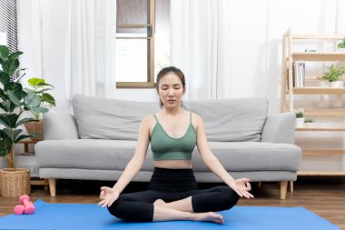 İnce Asyalı kadın evde yoga meditasyonu yapıyor, vücudun kaslarını esnetiyor ve düzgün nefes alma egzersizleri yapıyor, yoga stüdyosu, spor kıyafeti, sağlıklı yaşam tarzı, egzersiz konsepti..