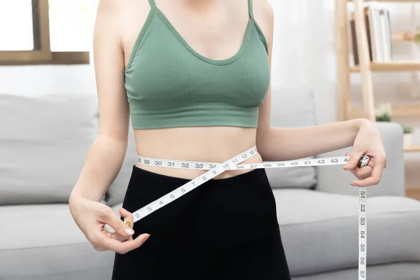 Woman in a gym clothes uses a centimeter strap to measure her circumference thin waist, Thin waist female, Health care concept and weight control, Sports waist, Healthy lifestyle, Physical activity.