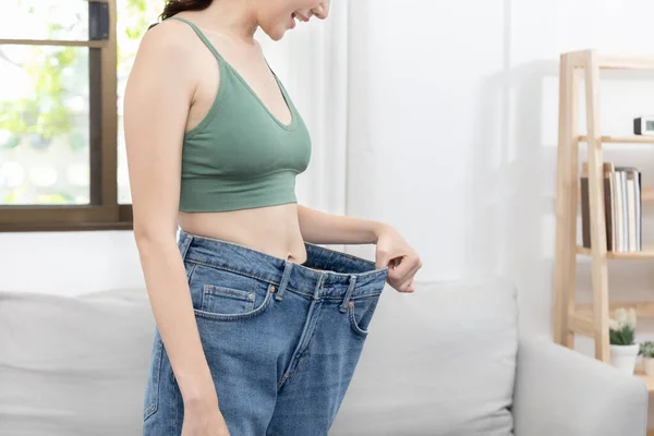 Women show a reduced or thinned waistline, Losing weight and exercising can reduce belly fat and excess fat, Loosing weight by keeping diet, Loose jeans, Body slim, Thin waist wearing big.