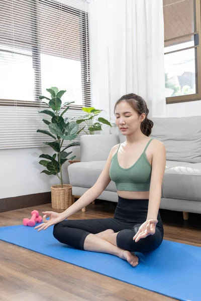 Slim Asian woman doing yoga meditation at home, Stretching the muscles of the body and practicing proper breathing, Yoga studio, Wearing sportswear, Healthy lifestyle, Exercise concept.