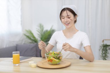 Yemek masasında salata yiyen Asyalı kadın gülümsüyor ve mutlu, sebze salataları vitamin ve mineraller, düşük kalorili ve yüksek lifli diyetler, taze sebze yiyerek sağlık hizmetleri açısından zengindir..