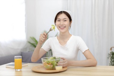 Yemek masasında salata yiyen Asyalı kadın gülümsüyor ve mutlu, sebze salataları vitamin ve mineraller, düşük kalorili ve yüksek lifli diyetler, taze sebze yiyerek sağlık hizmetleri açısından zengindir..
