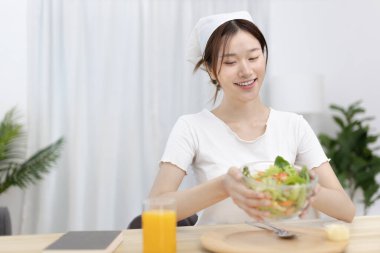 Yemek masasında salata yiyen Asyalı kadın gülümsüyor ve mutlu, sebze salataları vitamin ve mineraller, düşük kalorili ve yüksek lifli diyetler, taze sebze yiyerek sağlık hizmetleri açısından zengindir..