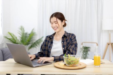Beautiful woman using on a laptop on a table with vegetable salad and freshly squeezed orange juice for breakfast, Morning break on weekends, Comfort zone, Happy relaxation,  Stay home.