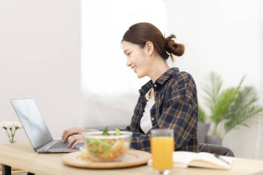 Beautiful woman using on a laptop on a table with vegetable salad and freshly squeezed orange juice for breakfast, Morning break on weekends, Comfort zone, Happy relaxation,  Stay home.