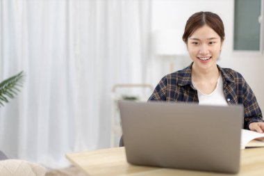 Not defterine not alan Asyalı kadın evde dizüstü bilgisayarda çalışırken, görüntülü sohbet, online iletişim, Evde kal, Yeni Normal, Mesafeli Öğrenme