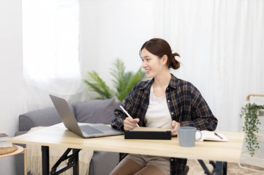Asian woman taking notes in notebook while studying online in laptop or tablet  at home, Video chat, Online communication , Stay home, New normal, Distance learnin
