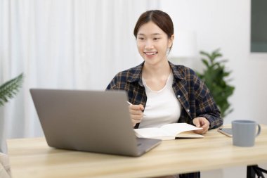 Not defterine not alan Asyalı kadın evde dizüstü bilgisayarda çalışırken, görüntülü sohbet, online iletişim, Evde kal, Yeni Normal, Mesafeli Öğrenme
