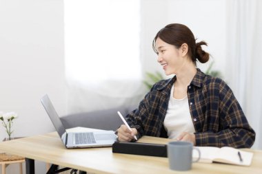 Asian woman taking notes in notebook while studying online in laptop or tablet  at home, Video chat, Online communication , Stay home, New normal, Distance learnin