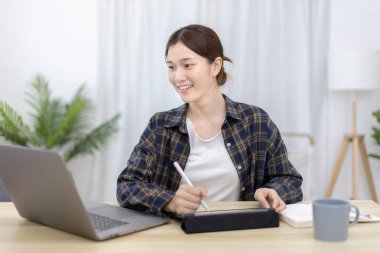 Asian woman taking notes in notebook while studying online in laptop or tablet  at home, Video chat, Online communication , Stay home, New normal, Distance learnin