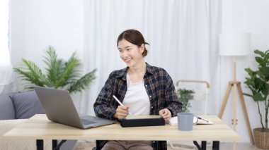 Asian woman taking notes in notebook while studying online in laptop or tablet  at home, Video chat, Online communication , Stay home, New normal, Distance learnin