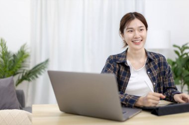 Asian woman taking notes in notebook while studying online in laptop or tablet  at home, Video chat, Online communication , Stay home, New normal, Distance learnin
