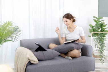 Asian woman taking notes in notebook while studying online in laptop at home, Video chat, Online communication , Stay home, New normal, Distance learning, Live show online, Learn online, living room.